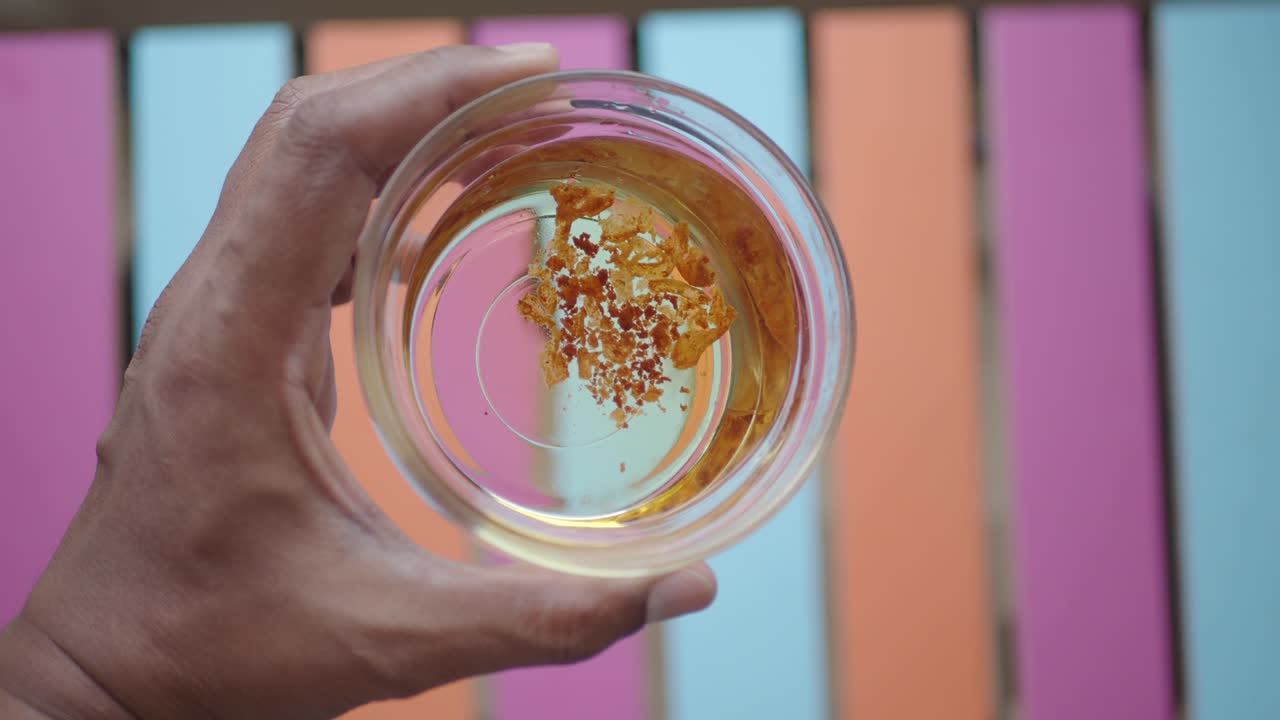 Primo piano di una mano che tiene una ciotola di vetro con zafferano in liquido