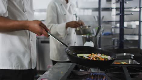 Midsection-of-mixed-race-male-chef-frying-vegetables-in-pan