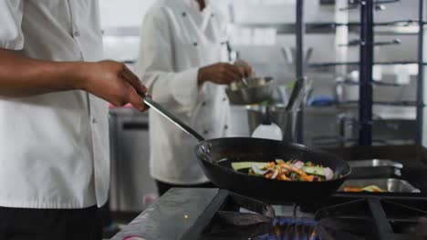 sección media de raza mixta chef masculino fritando verduras en sartén