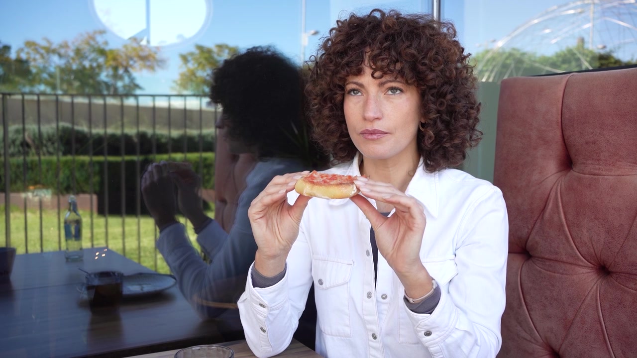 A thoughtful woman sitting in a cozy cafe sporting curly hair and gazing at a reflective window