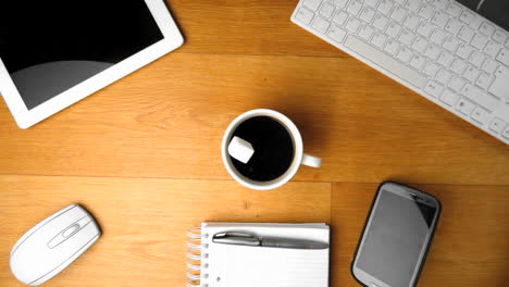 cubo de azúcar cayendo en una taza de café junto a la tableta pc y el teléfono inteligente