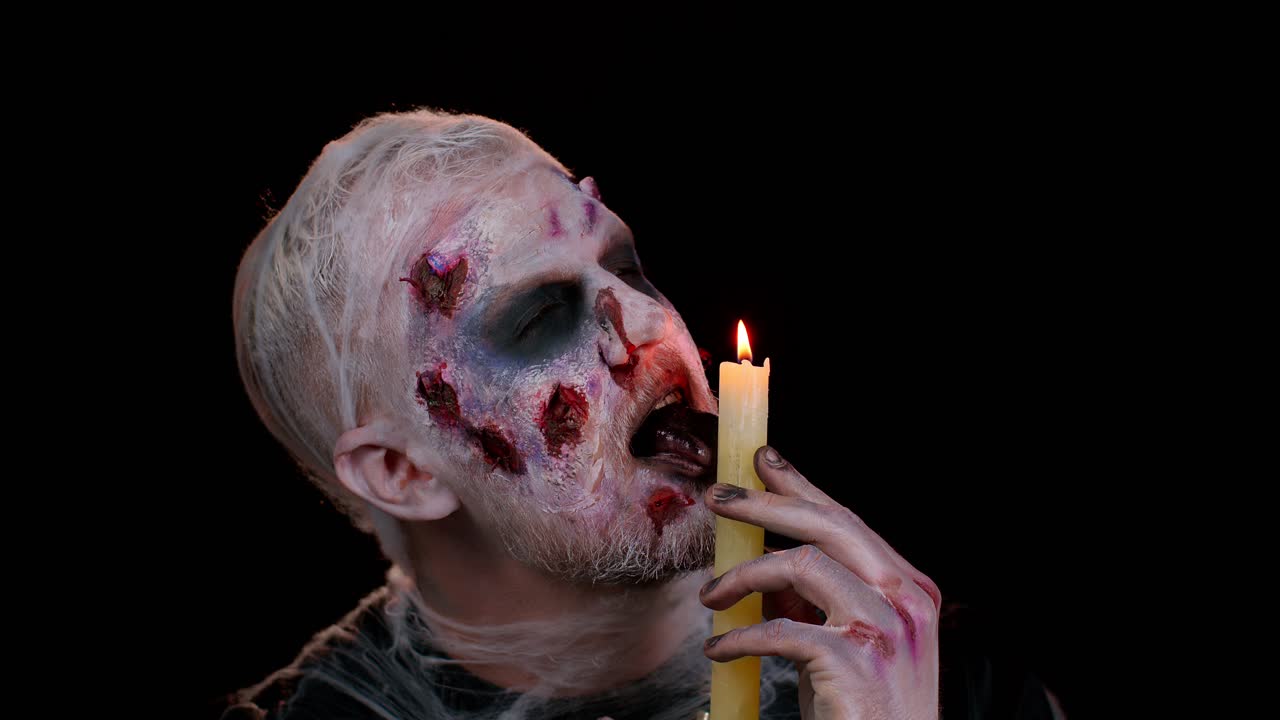 hombre con halloween zombie sangriento maquillaje herido, tratando de asustar, hechizos conjuros sobre una vela