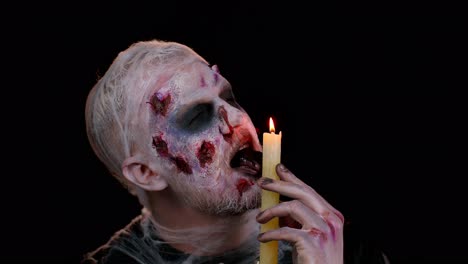 Man-with-Halloween-zombie-bloody-wounded-makeup,-trying-to-scare,-spells-conjures-over-a-candle