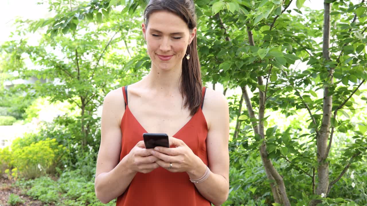 una joven alemana de cabello largo y marrón está escribiendo en su teléfono inteligente o móvil