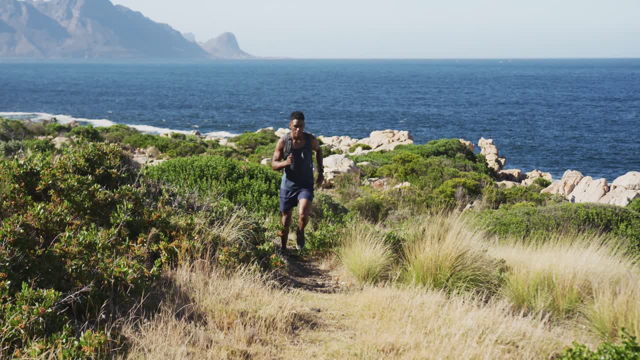 hombre afroamericano haciendo ejercicio al aire libre a través del país corriendo en el campo por la costa