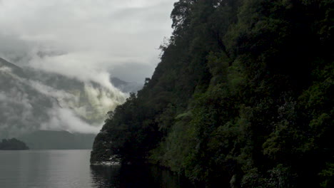 Slow-Motion-pan-across-mist-covered,-sun-dappled-mountains-in-Doubtful-Sound---Patea,-New-Zealand