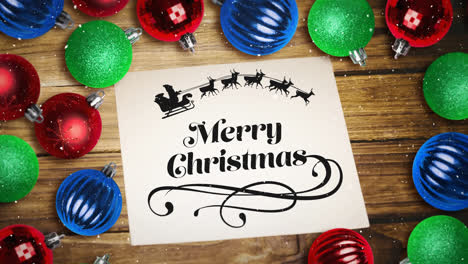 Falling-snow-and-Merry-Christmas-text-note-and-bauble-decorations-on-wood