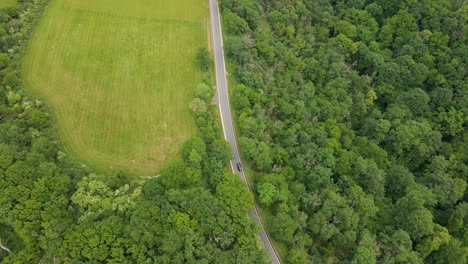 two cars driving along a curved country road in between lush meadows and leafy deciduous forests in rhineland palatinate, germany