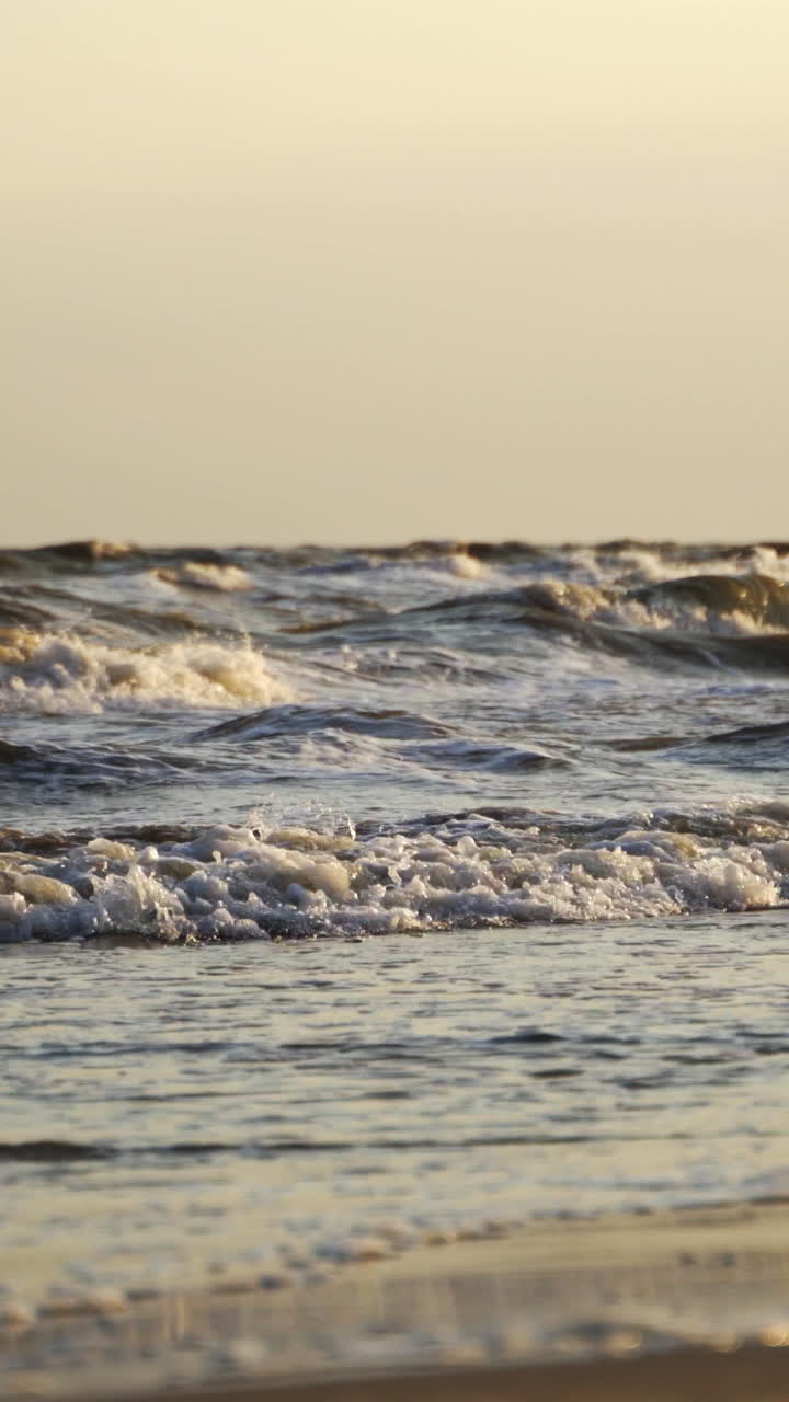 Wave drops at the beach. Close up view of sea water waves with bubbles on sand beach Vertical video
