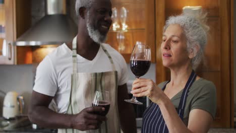 pareja de alto nivel de raza mixta brindando y bebiendo vino juntos en la cocina en casa