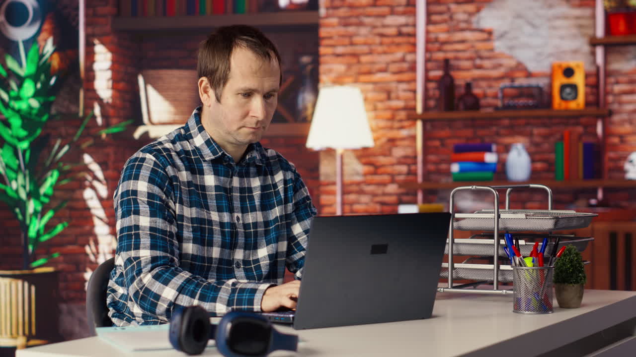 Man seated at home office desk using laptop, checking emails