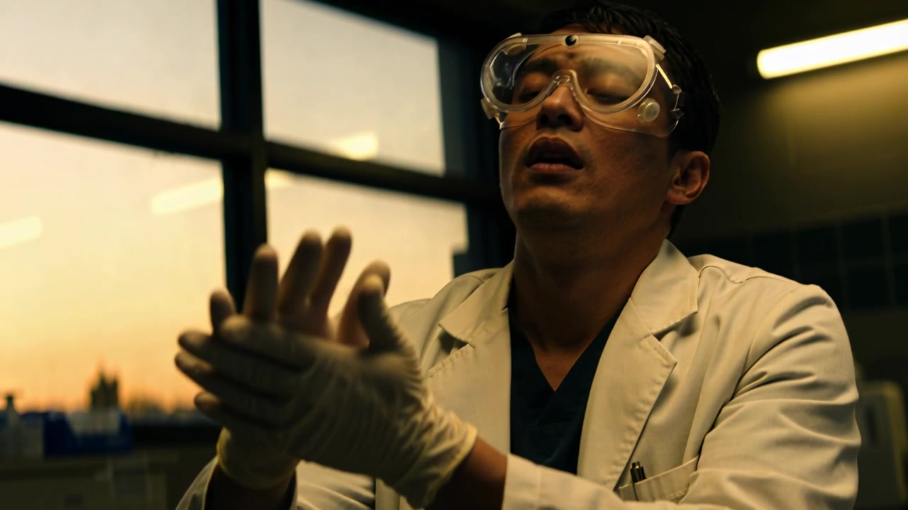 Lab scientist in white coat donning latex gloves and adjusting goggles at lab bench, preparing task