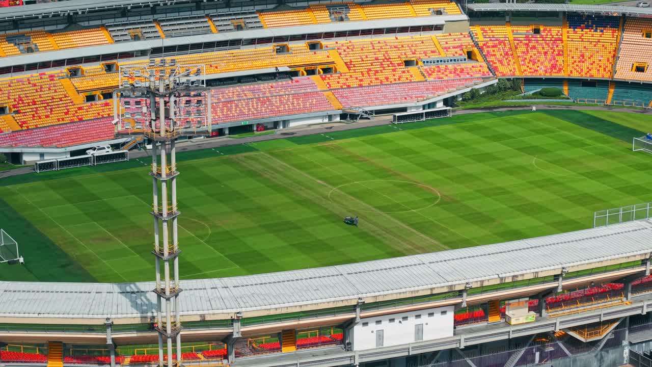 Aerial orbit establishing a person with heavy machinery mowing the lawn of the empty El Campin stadium in Bogota, Colombia on a sunny day.