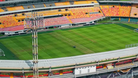 aerial orbit establishing a person with heavy machinery mowing the lawn of the empty el campin stadium in bogota, colombia on a sunny day.
