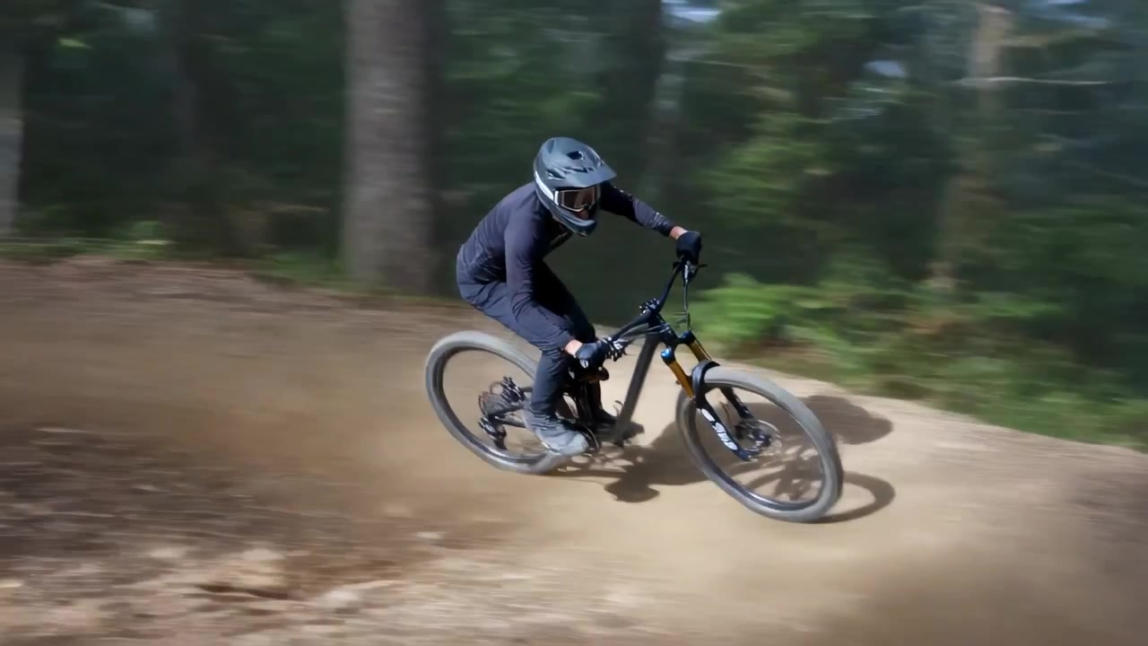 Ciclista con casco in bicicletta che entra in un sentiero nebbioso nel bosco per scendere, passando un segnale e sollevando polvere.