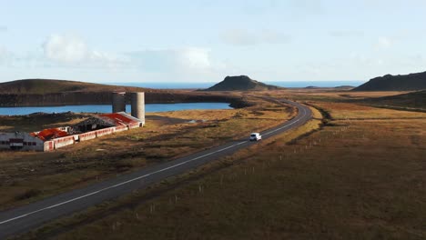 el coche viaja por una carretera rural remota pasando por un edificio agrícola abandonado, la luz del sol de la hora dorada, una toma cinematográfica