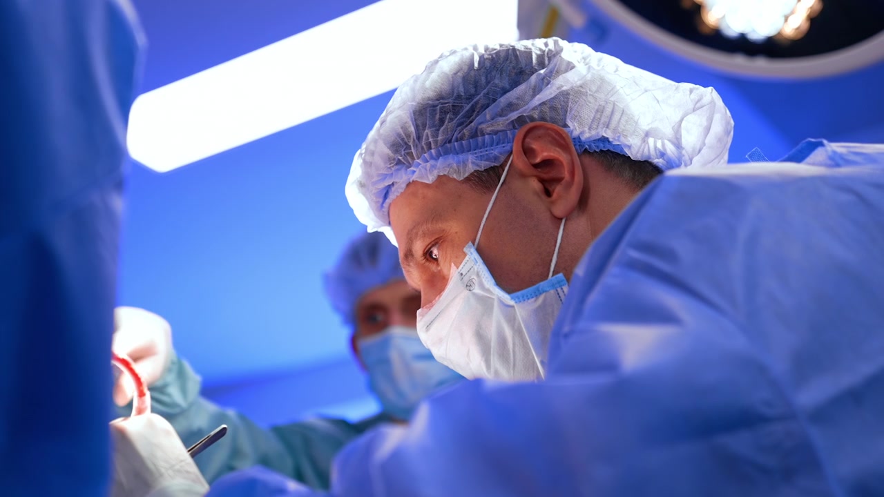 Sguardo concentrato di un chirurgo caucasico uomo con maschera e cuffia che tiene gli strumenti. Vista dal basso sul dottore che esegue la neurochirurgia.