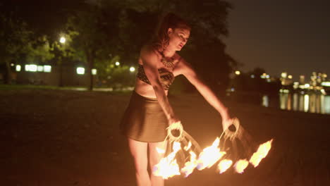 Mujer-Bailando-Con-Abanicos-De-Fuego-En-La-Playa-Junto-Al-Lago-Contra-El-Horizonte-De-Toronto,-Tiro-Medio-Exterior-Nocturno