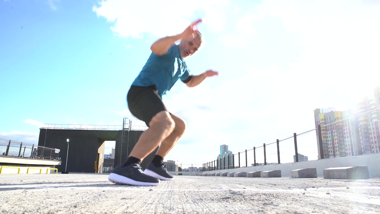 Uomo maturo che corre ed esegue burpees su un tetto urbano