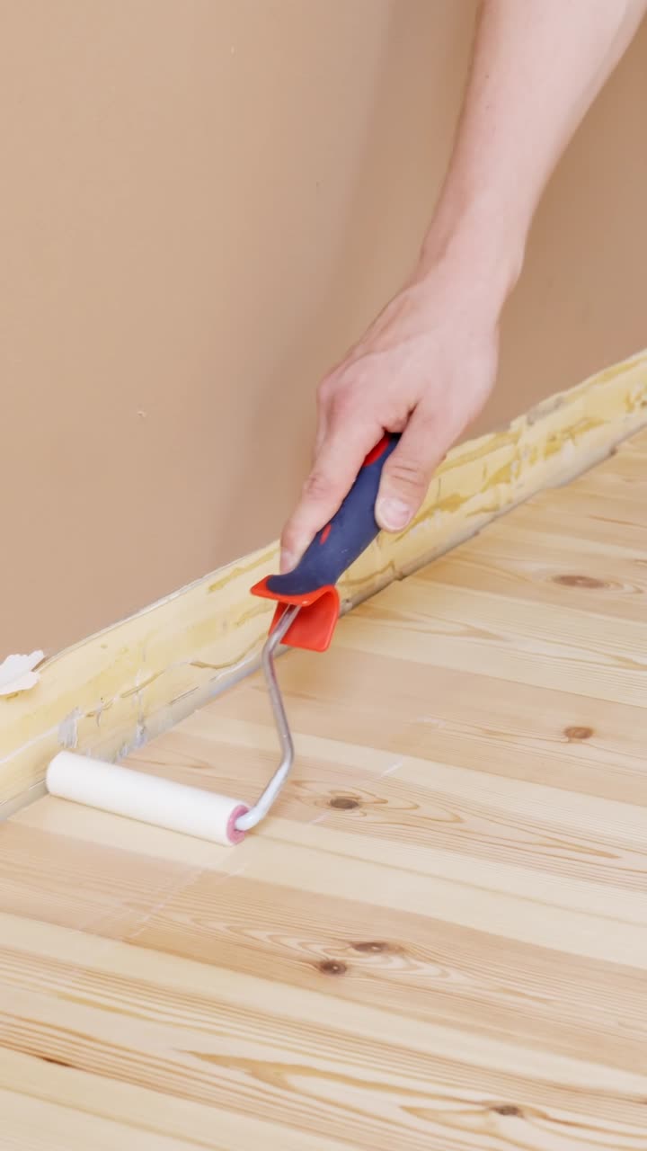 Hand applying varnish to a hardwood floor edge with a small roller, vertical
