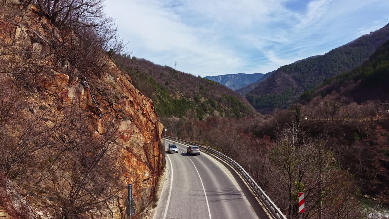 Dağlık bölgede, kayalık tepelerin arasından geçen virajlı yol, gündüz vakti açık gökyüzü ve az bulutla.