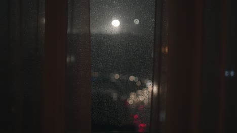 rain and storm seen through the window glass and curtains with muted traffic and city light by night