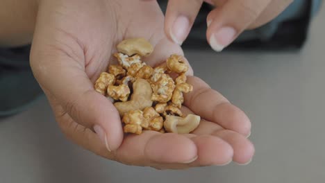 a woman's hand holding a handful of cashews and caramel corn