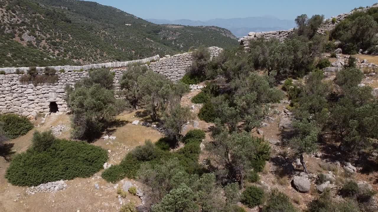 Pedestal drone shot moving from the bottom going up, showing a wall along the Lycian Way's hiking trail and revealing a modern Turkish town below, located in the province of Antalya, Turkey