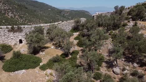 pedestal drone shot moving from the bottom going up, showing a wall along the lycian way's hiking trail and revealing a modern turkish town below, located in the province of antalya, turkey