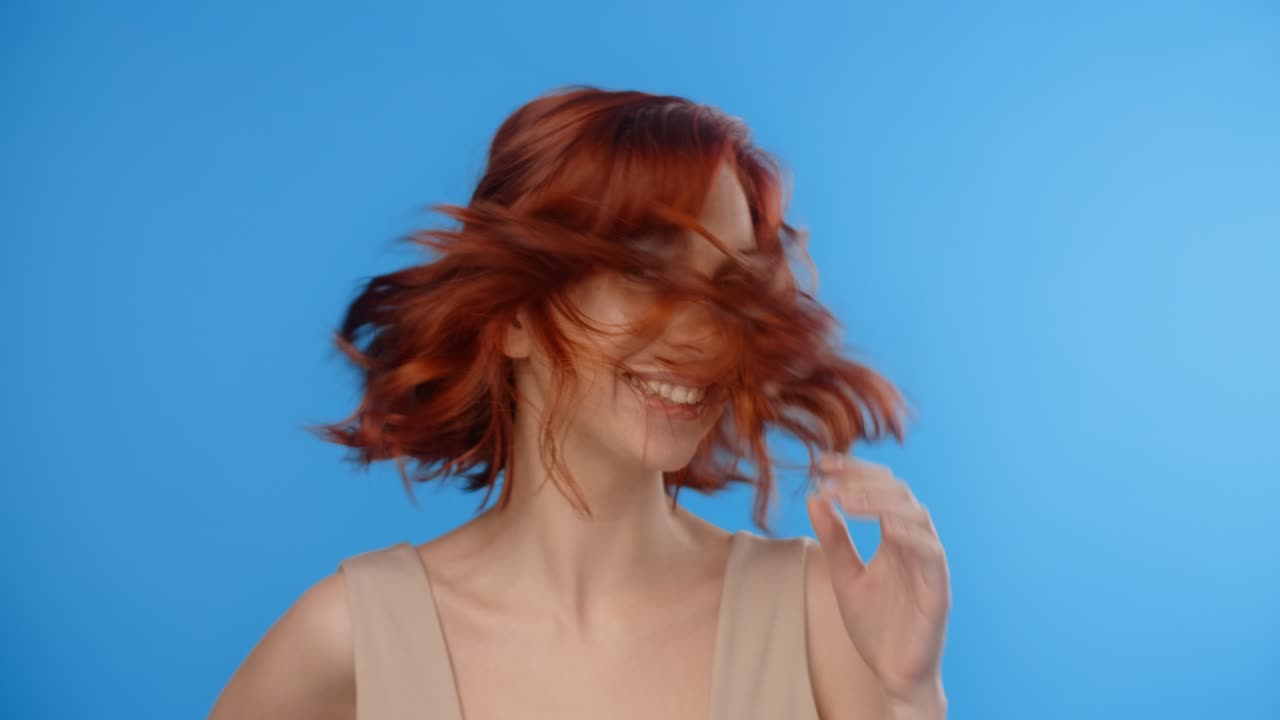 은 머리의 예쁜 여자가 머리를 굴리고 파란 스크린에 머리를 던집니다. 모델은 사진 촬영에서 머리카락을 던졌습니다.