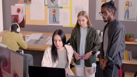 young female graphic designer explaining project on computer to her multiethnic colleagues in an animation studio