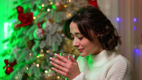 warm drink by the tree. a woman enjoys a warm drink while sitting near a beautifully decorated christmas tree with festive lights