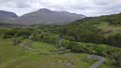 an aerial view over curvy rural road following it's curves and a car passing, river flowing on a dark grey day in ireland