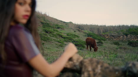 Young-woman-standing-pasture-looking-on-cute-cow-gazering-eating-green-grass.