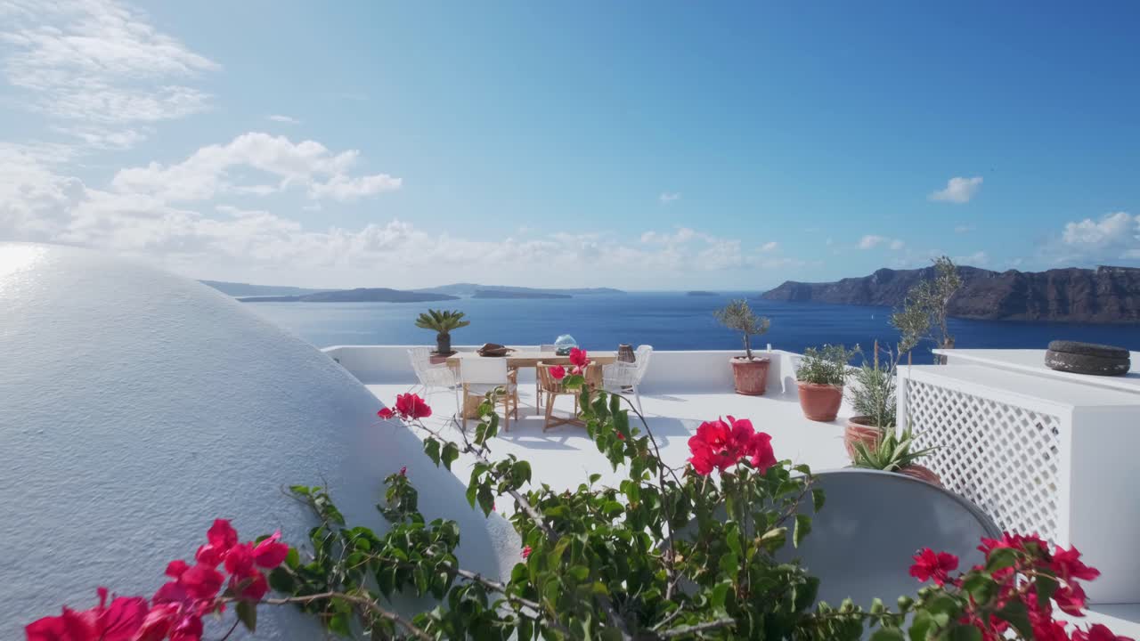 mesa con sillas en un balcón blanco con flores rosas en primer plano