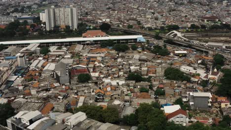 Aerial-tilt-down-shot-of-slum-district-near-highway-in-Jakarta-city,-capital-of-Indonesia