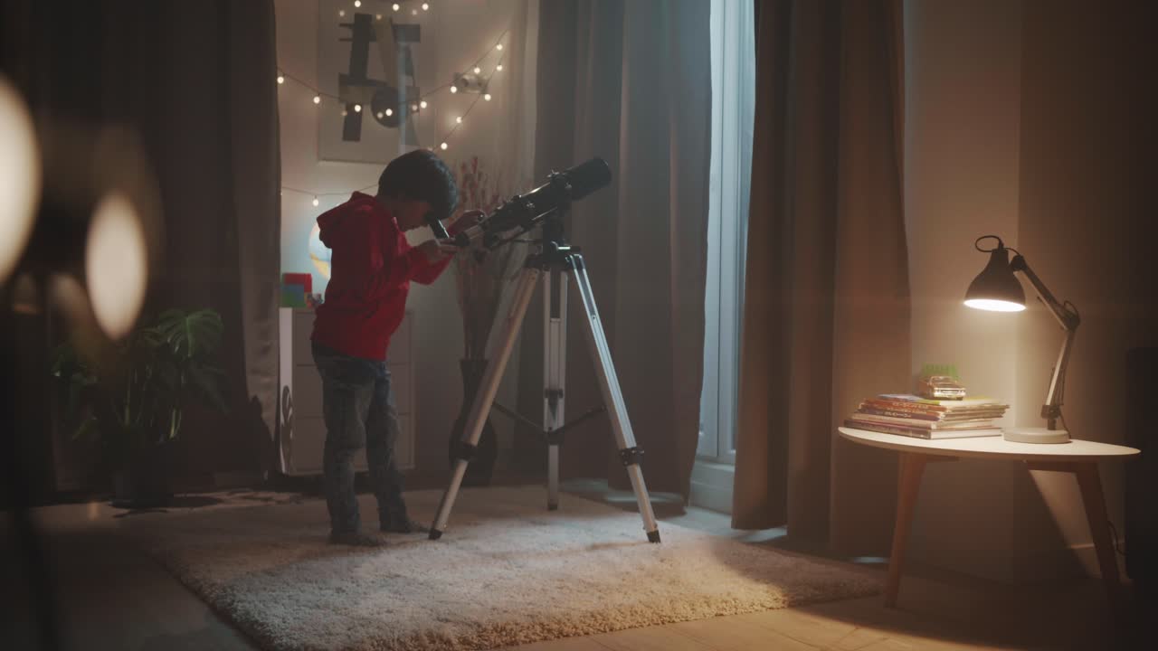 A curious young boy uses a telescope in his room at night to explore the stars. A concept of childhood dreams, science education, an astronomy hobby, and inspiring wonder