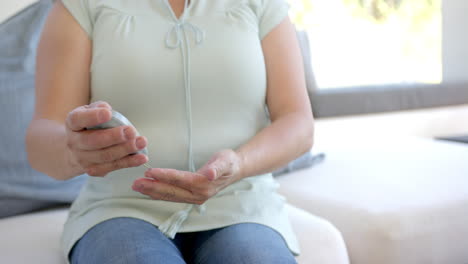 Applying lotion to hands, asian woman sitting on couch in comfortable home setting