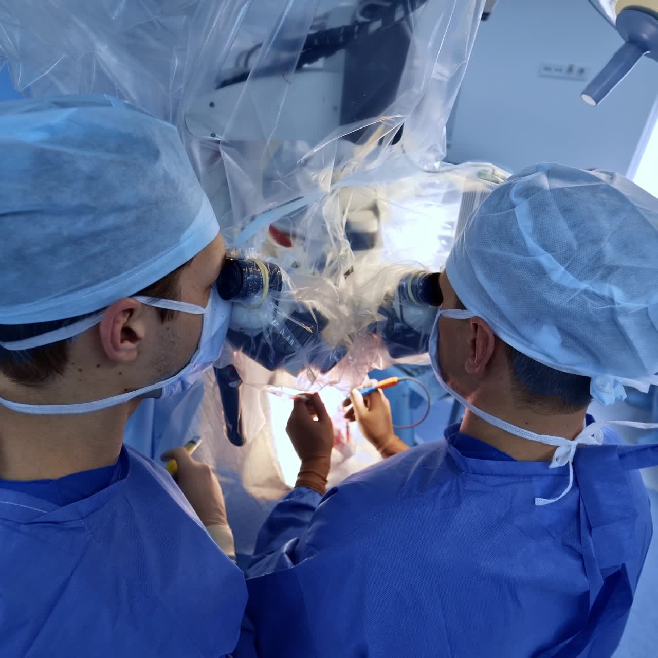 Neurosurgical team carrying out the surgery in modern hospital. Main surgeon looks at operated area through the advanced microscope. Top view