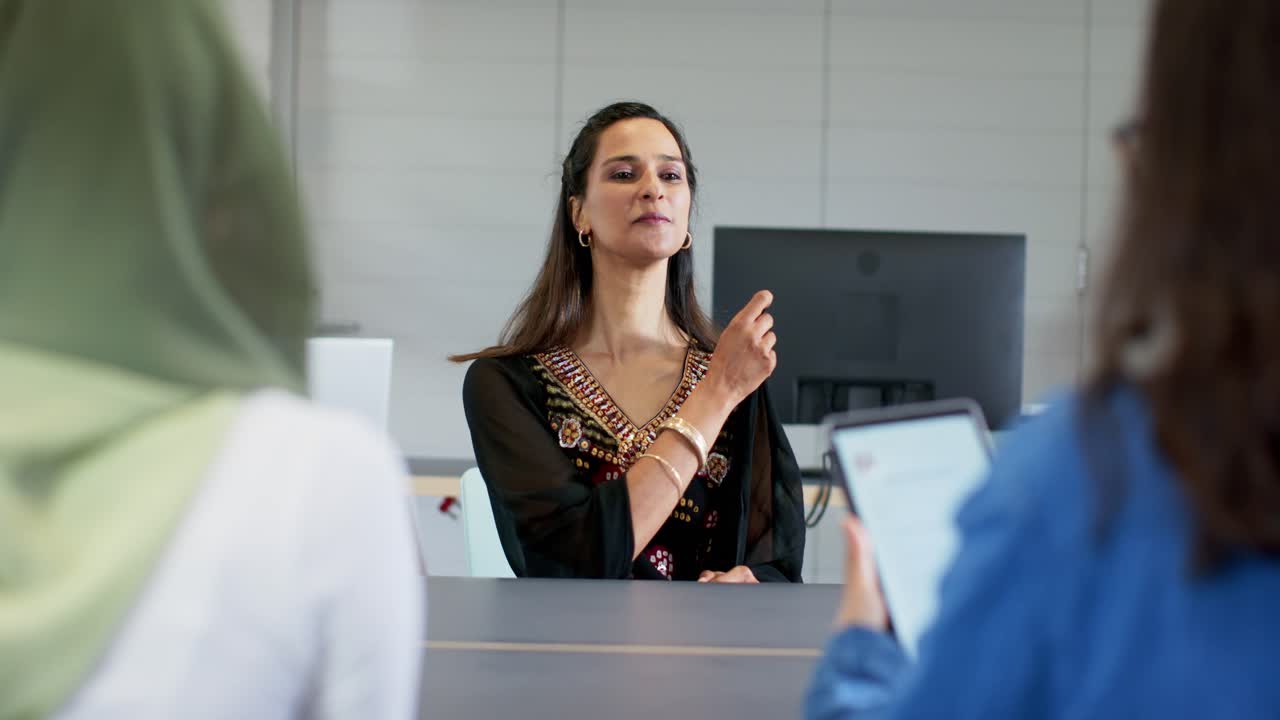 Indian woman hearing interviewer question, responding confidently with laptop at conference table