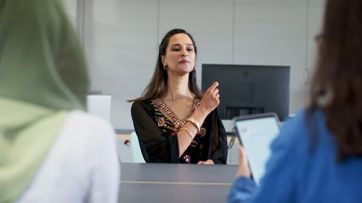 Indian woman hearing interviewer question, responding confidently with laptop at conference table