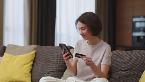 joven feliz tiene tarjeta de crédito bancaria, teléfono, usando aplicación bancaria, hace compras en casa. compras en línea, comercio electrónico