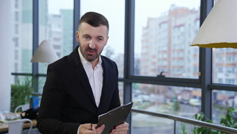 middle-aged businessman talking to his employees sitting in front of him. man speaking, gesturing and showing the graphs. cityscape at the backdrop.