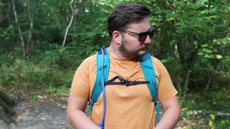 young man with a backpack and sunglasses lost alone in the woods looks at the compass and walks away