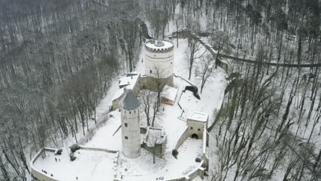 Drone-aerial-of-the-fairy-tale-castle-Plesse-in-winter-with-a-huge-amount-of-snow-on-a-beautiful-mountain-near-Bovenden,-Germany,-Europe