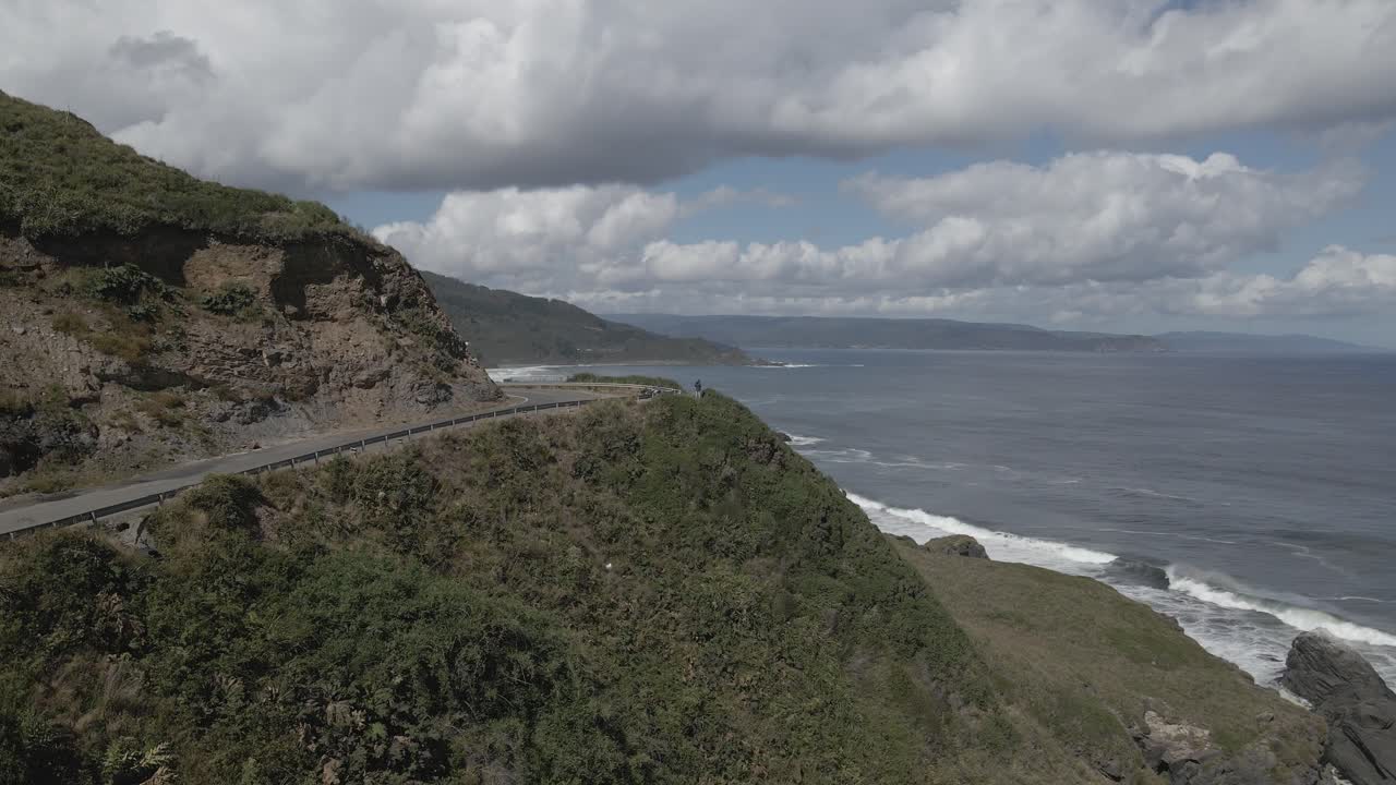 공중 높은 fps 푸시 ijn은 흐린 날에 파도를 타고 녹색 절벽 옆 해변을 촬영했습니다.