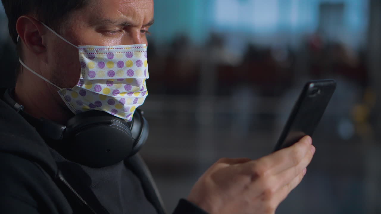 hombre con máscara y auriculares usando teléfono en el aeropuerto
