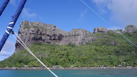 panning from sailboat: steep rock cliff on tropical polynesian island