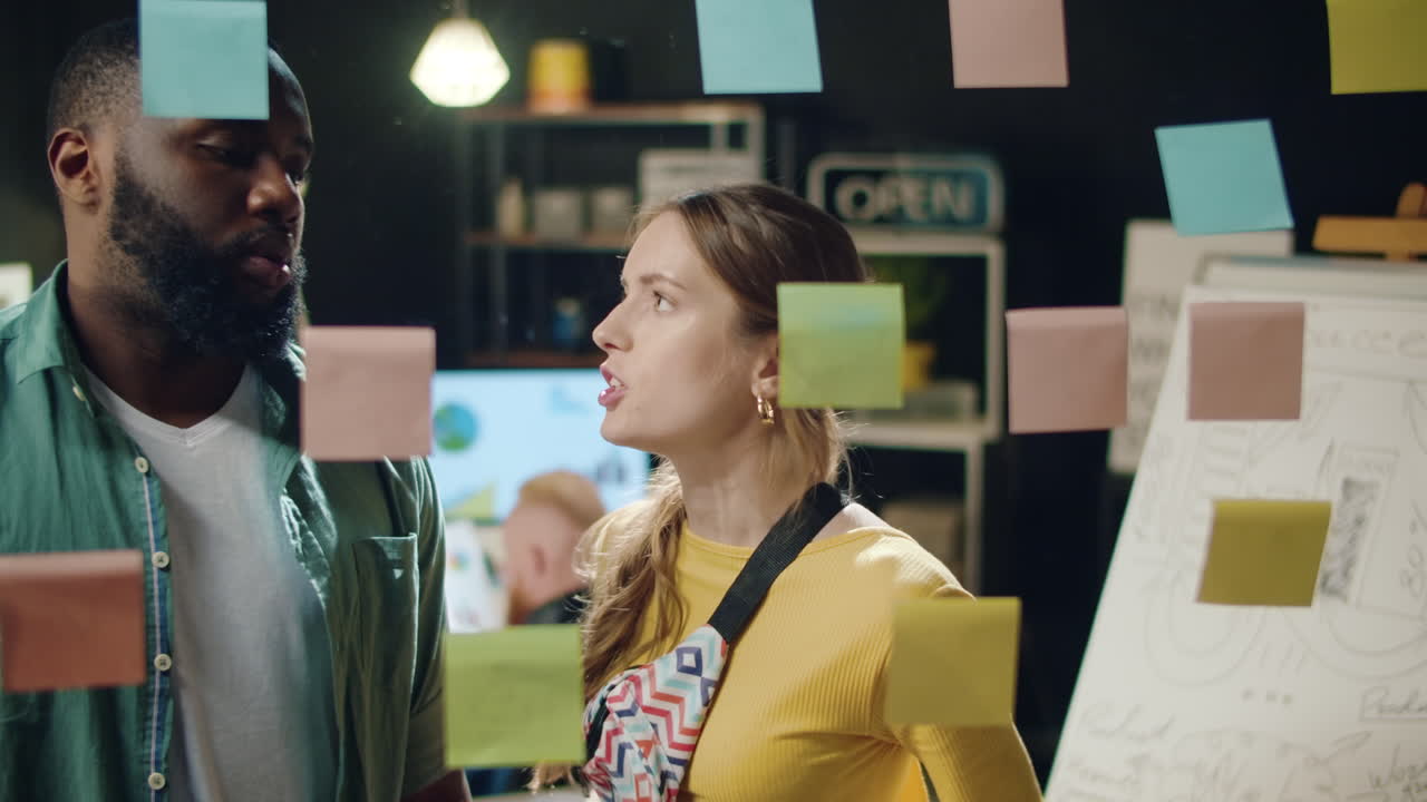 una pareja de raza mixta discutiendo en una oficina hipster. una mujer estresada quitando pegatinas