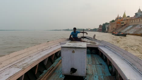 cinematic ancient holy city varanasi india ganges river man captain canal boat driver cruise northern state people on steps ghat pradesh province landscape gray cloudy fire smoke follow forward